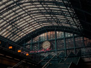 Large train station interior with a glass roof, grand clock, and neon red sign—pest control ensures the space stays welcoming for all.