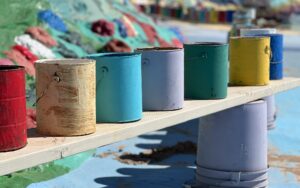 A row of paint cans sits on a wooden plank, with vibrant colors hinting at creative spaces safe from pests due to pest control.