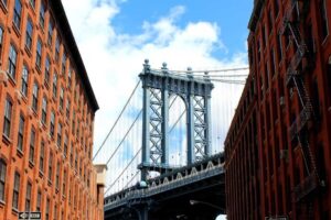 View of the Manhattan Bridge framed by two red brick buildings, where top-notch pest control keeps the cityscape pristine under a blue sky.