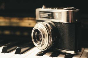 A vintage camera rests on piano keys, its lens and details softly lit, capturing a scene untouched by time or the need for pest control.